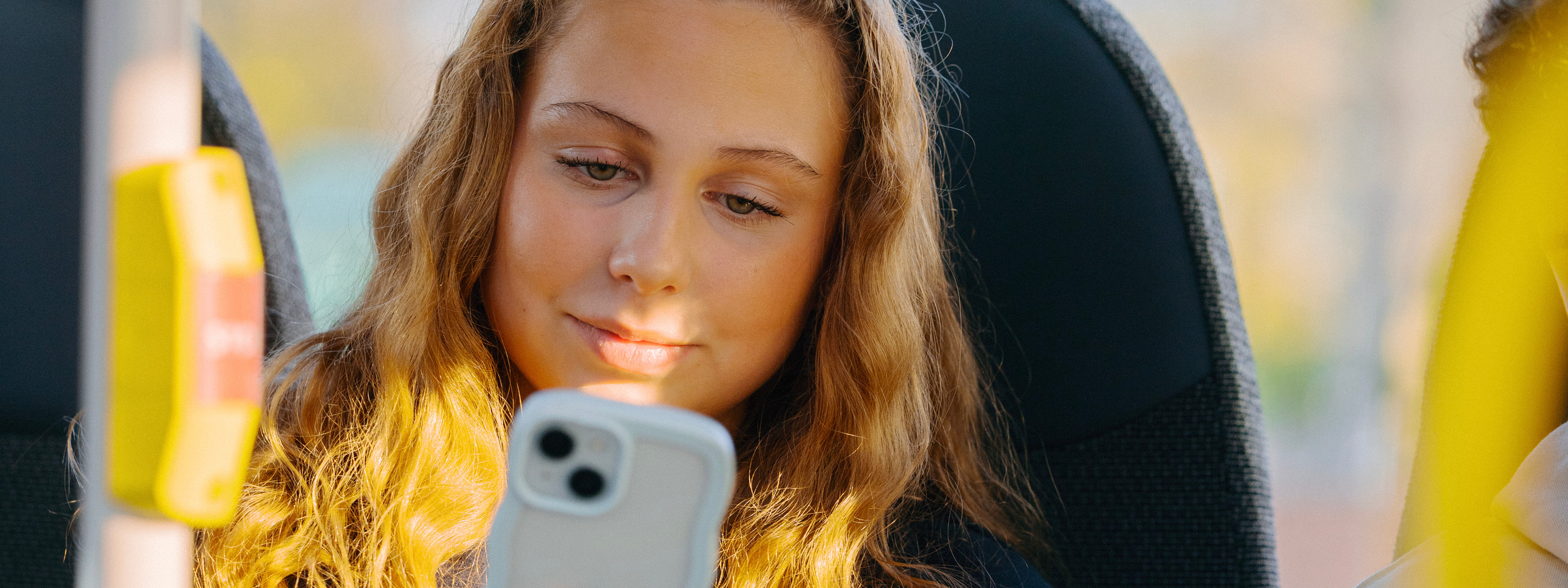 Tjej sitter i en buss. Hon ler och kollar i sin mobiltelefon.