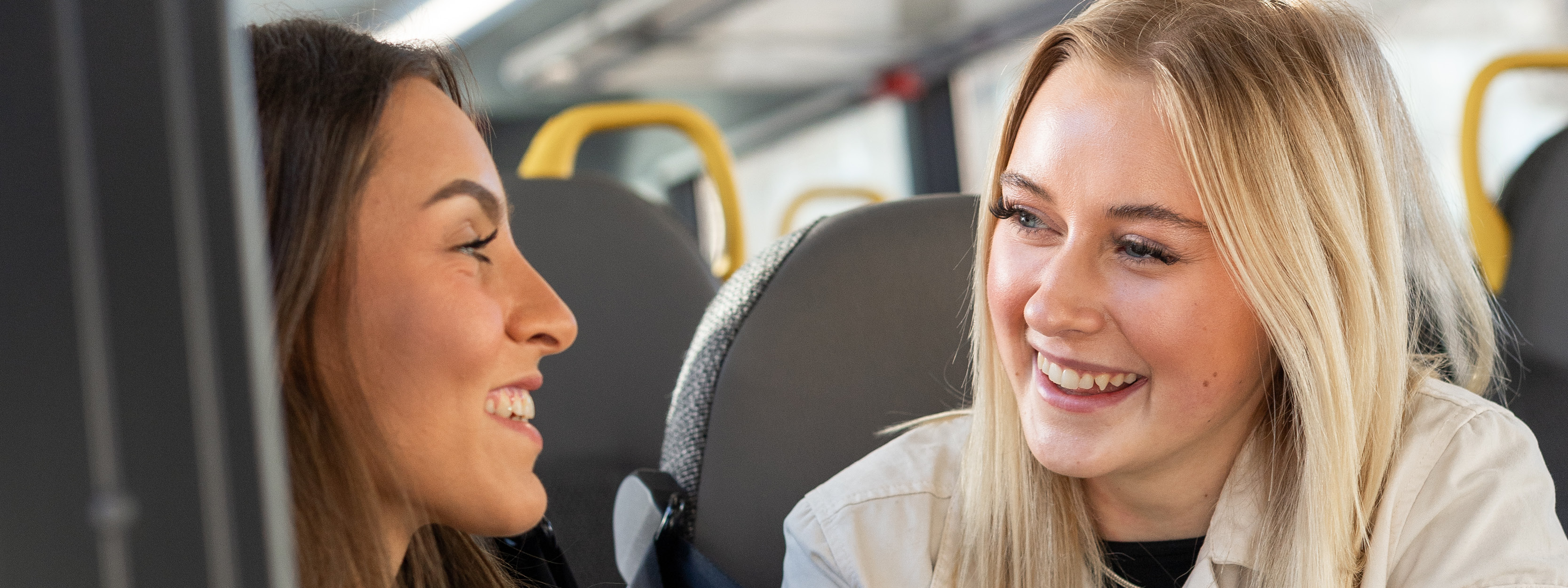 Två tjejer sitter på en buss. De ler mot varandra.